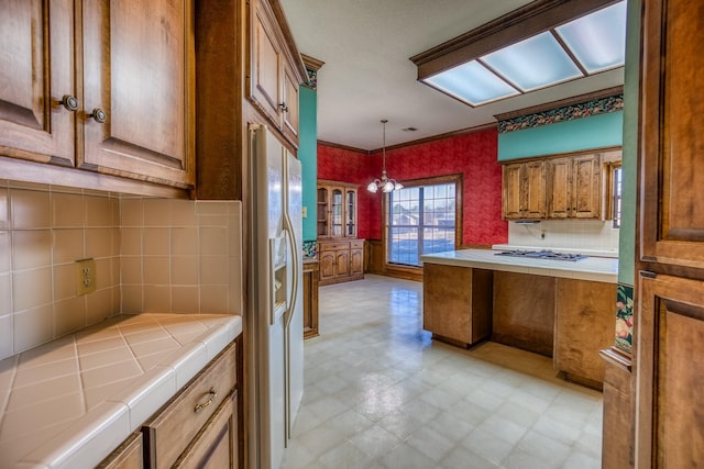 kitchen with tile countertops, hanging light fixtures, white refrigerator with ice dispenser, a notable chandelier, and crown molding