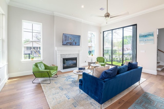 living room featuring crown molding, a high end fireplace, plenty of natural light, and light hardwood / wood-style floors