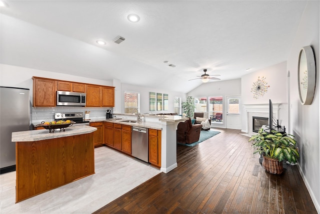 kitchen featuring sink, stainless steel appliances, light hardwood / wood-style floors, vaulted ceiling, and kitchen peninsula