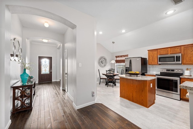 kitchen with wood-type flooring, decorative light fixtures, a kitchen island, stainless steel appliances, and backsplash