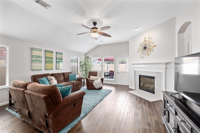 living room with dark wood-type flooring, ceiling fan, a high end fireplace, and vaulted ceiling