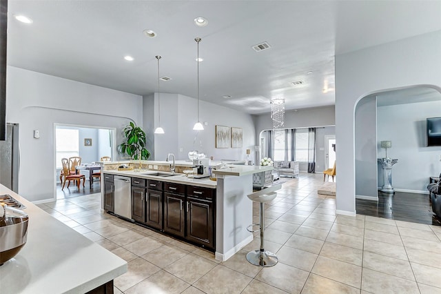 kitchen featuring a kitchen island with sink, decorative light fixtures, dark brown cabinetry, and light tile patterned flooring