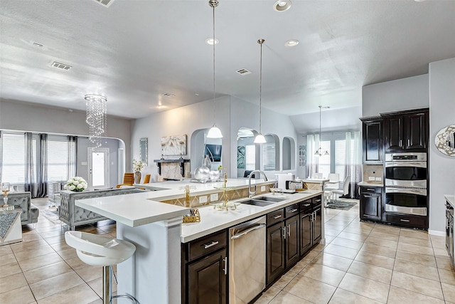 kitchen with a breakfast bar, sink, hanging light fixtures, a center island with sink, and appliances with stainless steel finishes