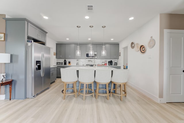 kitchen featuring hanging light fixtures, appliances with stainless steel finishes, a kitchen island with sink, and gray cabinets