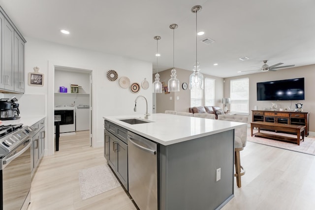 kitchen with gray cabinets, appliances with stainless steel finishes, a kitchen island with sink, and sink