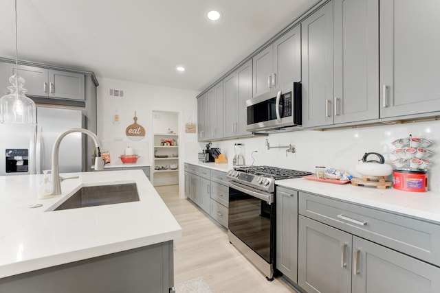 kitchen featuring sink, gray cabinets, stainless steel appliances, light hardwood / wood-style floors, and decorative light fixtures