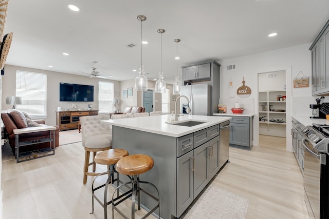 kitchen with appliances with stainless steel finishes, sink, a kitchen island with sink, and gray cabinetry