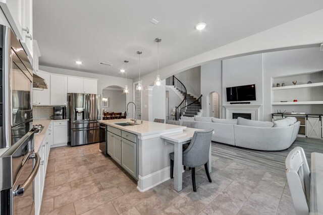 kitchen with decorative light fixtures, white cabinetry, sink, stainless steel appliances, and a center island with sink