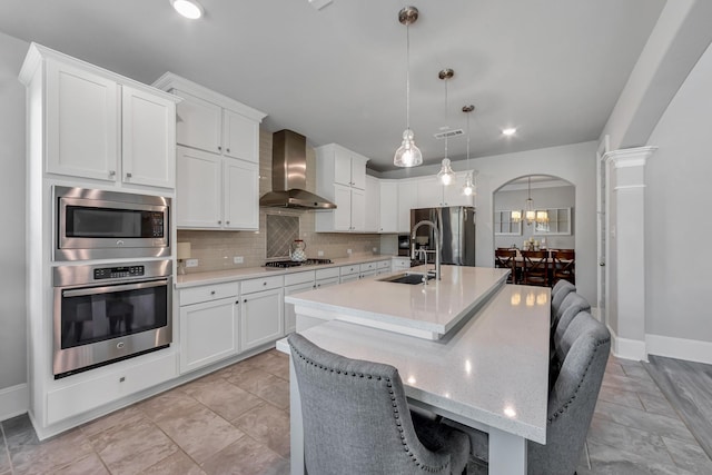 kitchen with appliances with stainless steel finishes, white cabinetry, hanging light fixtures, a kitchen bar, and wall chimney exhaust hood