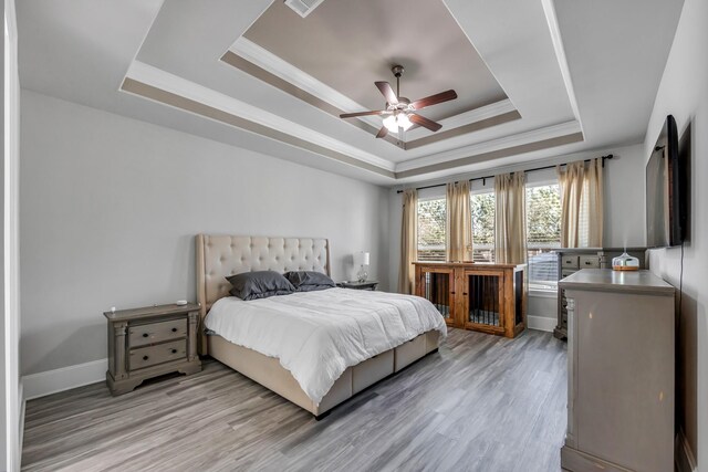 bedroom featuring light hardwood / wood-style flooring, ornamental molding, a raised ceiling, and ceiling fan