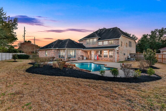 back house at dusk with a fenced in pool, a patio area, a balcony, and a lawn