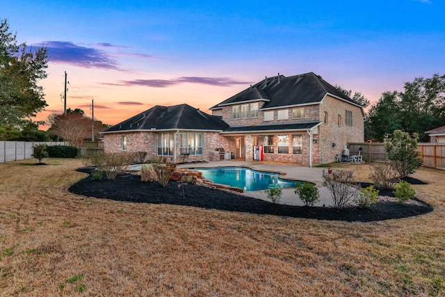 back house at dusk with a balcony, a yard, a fenced in pool, and a patio area