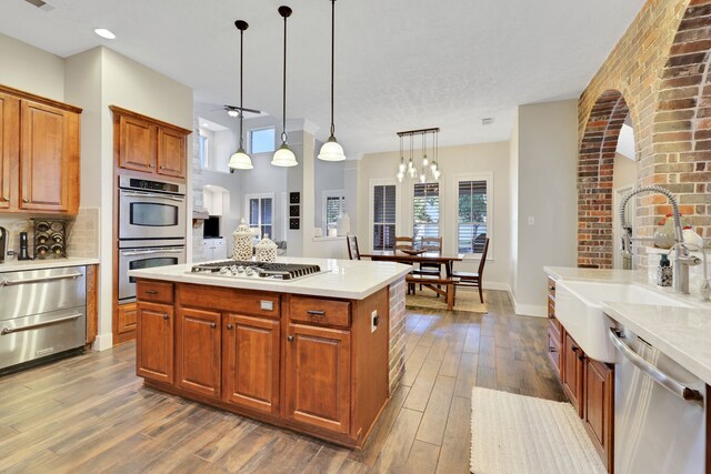 kitchen with sink, hanging light fixtures, a kitchen island, stainless steel appliances, and backsplash