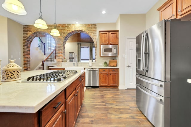 kitchen featuring brick wall, dark hardwood / wood-style floors, decorative light fixtures, sink, and stainless steel appliances