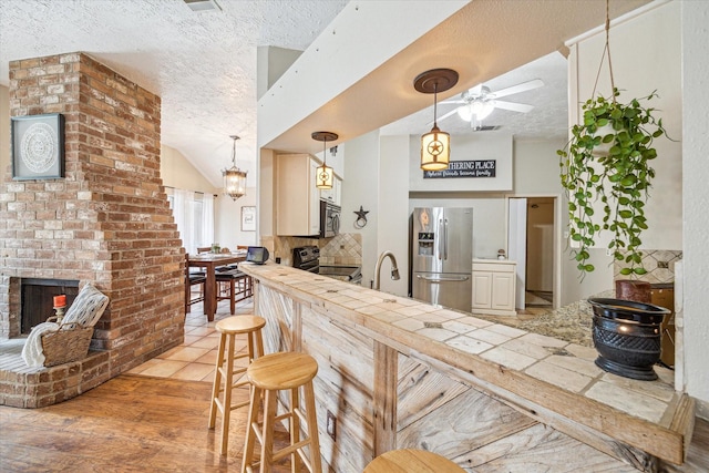 kitchen with a brick fireplace, a textured ceiling, appliances with stainless steel finishes, and light wood-style flooring