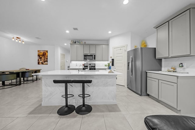 kitchen featuring appliances with stainless steel finishes, a center island with sink, and gray cabinetry