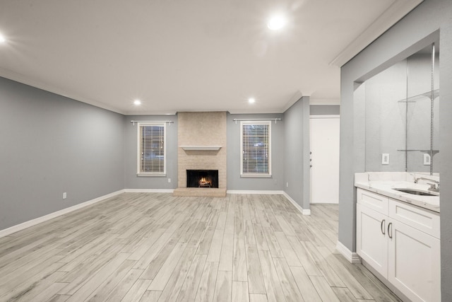 unfurnished living room with sink, a fireplace, ornamental molding, and light wood-type flooring