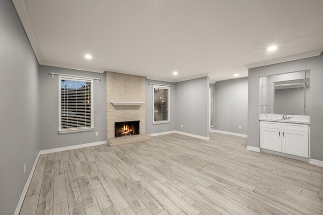 unfurnished living room with ornamental molding, a fireplace, sink, and light hardwood / wood-style flooring