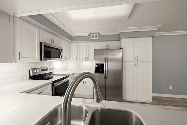 kitchen with light stone countertops, crown molding, stainless steel appliances, and white cabinets