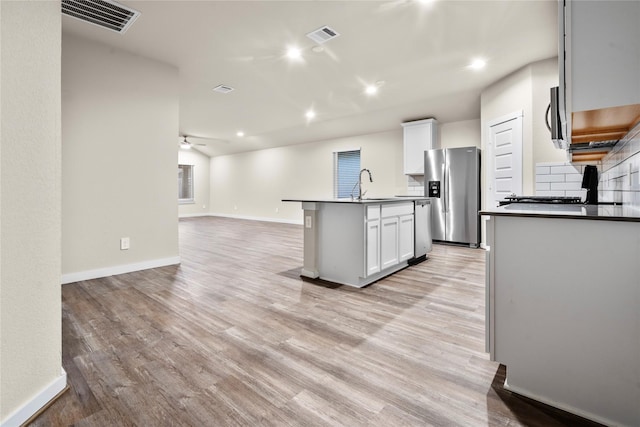 kitchen with appliances with stainless steel finishes, a kitchen island with sink, white cabinets, and light hardwood / wood-style flooring