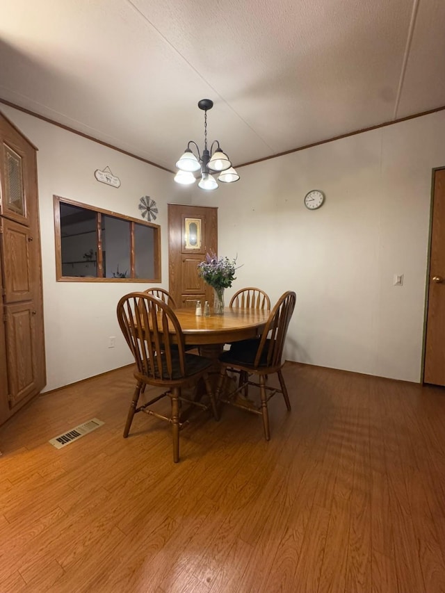 dining space with ornamental molding, an inviting chandelier, a textured ceiling, and light hardwood / wood-style floors