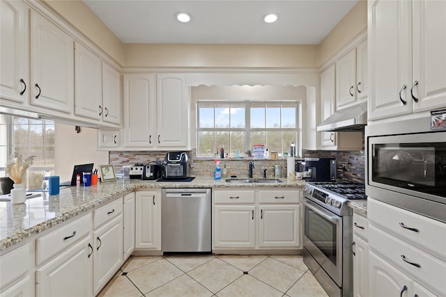 kitchen with sink, light tile patterned floors, appliances with stainless steel finishes, light stone countertops, and white cabinets