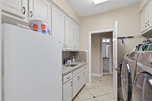 clothes washing area with sink, light tile patterned floors, cabinets, and washer and dryer