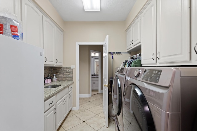 laundry area featuring sink, cabinets, washer and dryer, a textured ceiling, and light tile patterned flooring