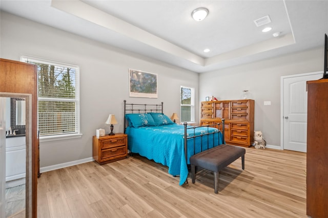 bedroom featuring baseboards, visible vents, light wood finished floors, and a raised ceiling