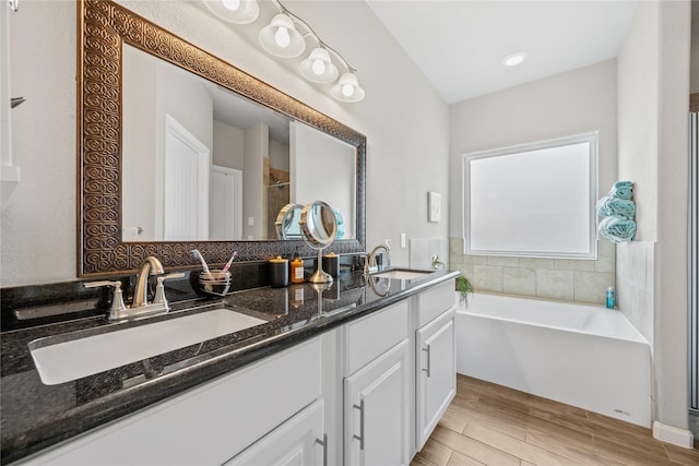 bathroom with double vanity, a bath, wood finished floors, and a sink
