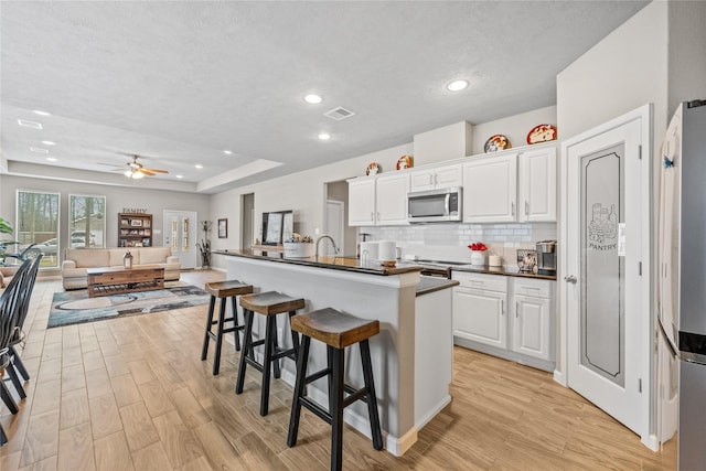 kitchen featuring dark countertops, light wood-style flooring, stainless steel microwave, and a breakfast bar area