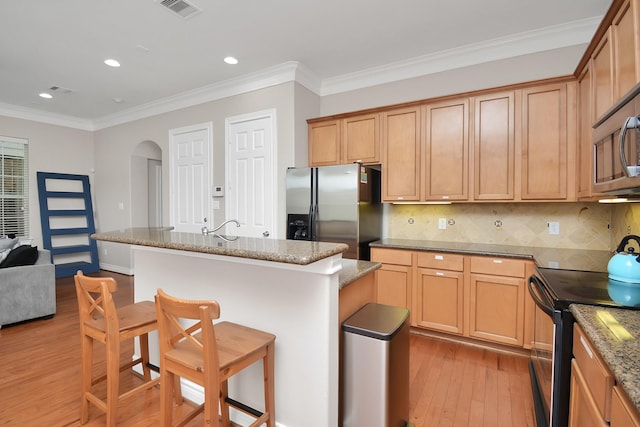 kitchen with crown molding, light hardwood / wood-style flooring, appliances with stainless steel finishes, an island with sink, and light stone countertops