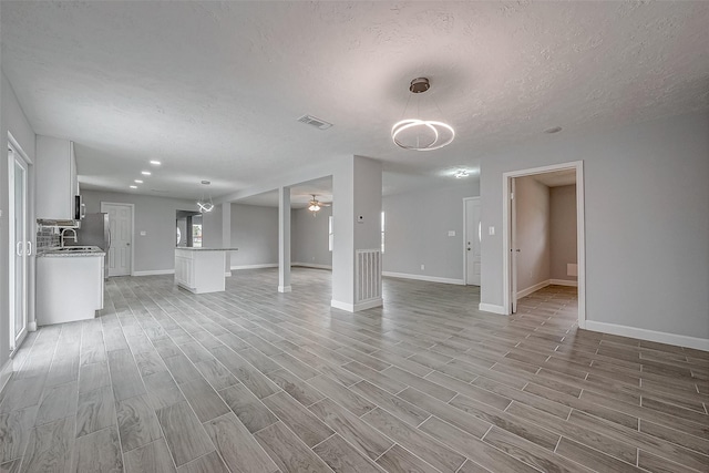 unfurnished living room with sink, a textured ceiling, ceiling fan, and light hardwood / wood-style flooring