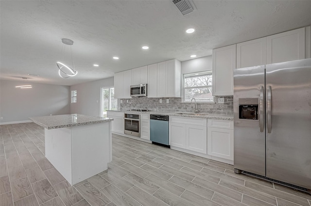 kitchen featuring pendant lighting, stainless steel appliances, sink, and white cabinets