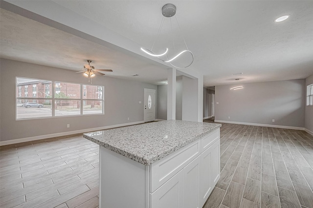 kitchen with decorative light fixtures, white cabinetry, ceiling fan, light stone counters, and a textured ceiling