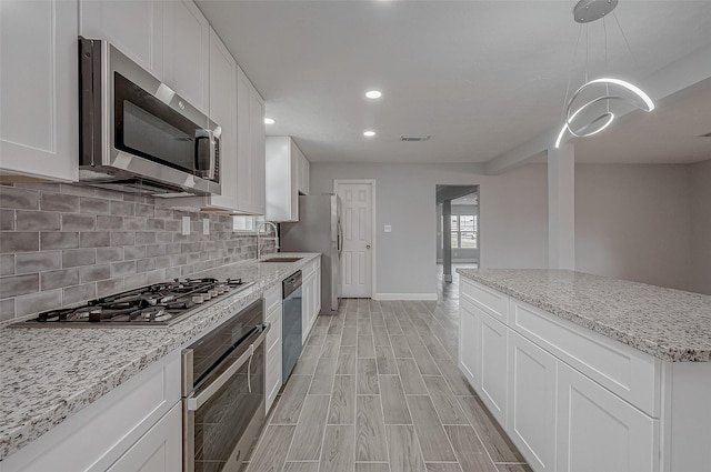 kitchen with sink, appliances with stainless steel finishes, white cabinetry, backsplash, and decorative light fixtures