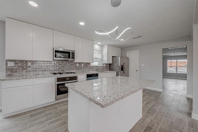 kitchen featuring sink, white cabinetry, a center island, appliances with stainless steel finishes, and pendant lighting