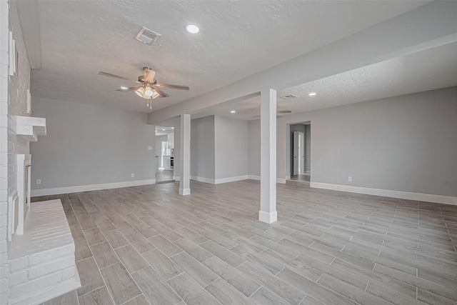 basement featuring ceiling fan, a fireplace, a textured ceiling, and light hardwood / wood-style flooring