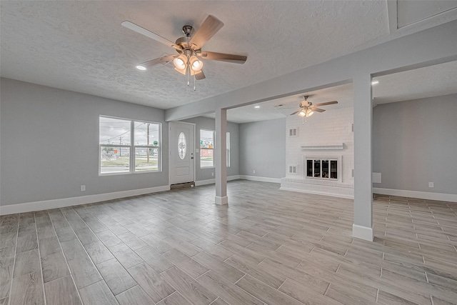 unfurnished living room with ceiling fan, a textured ceiling, and a fireplace