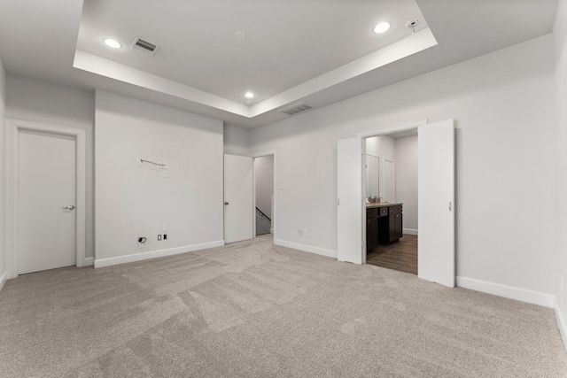 unfurnished bedroom with carpet flooring, ensuite bathroom, and a tray ceiling