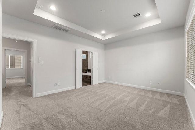 unfurnished bedroom featuring a raised ceiling, ensuite bathroom, and carpet flooring