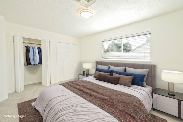 bedroom with multiple closets, light colored carpet, and a textured ceiling