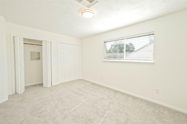 unfurnished bedroom with multiple closets, light colored carpet, and a textured ceiling