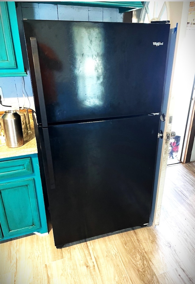 details with light hardwood / wood-style floors and black refrigerator