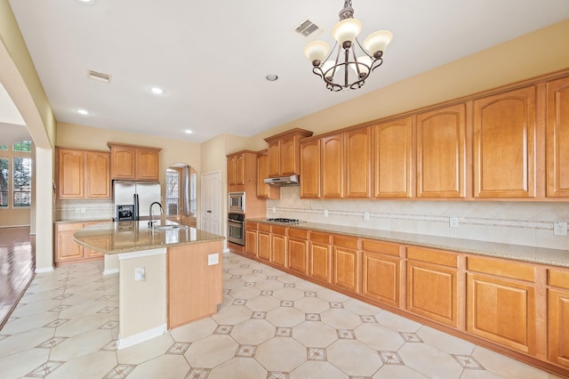 kitchen featuring sink, light stone counters, hanging light fixtures, a center island with sink, and stainless steel appliances