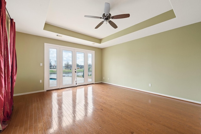 empty room featuring hardwood / wood-style flooring, ceiling fan, and a raised ceiling