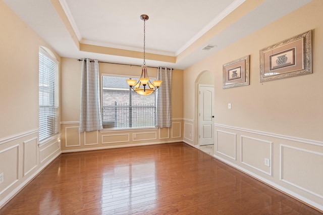 unfurnished dining area with hardwood / wood-style floors, a notable chandelier, ornamental molding, and a raised ceiling