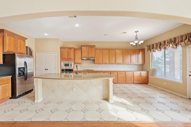 kitchen with stainless steel appliances, tasteful backsplash, a center island with sink, and decorative light fixtures