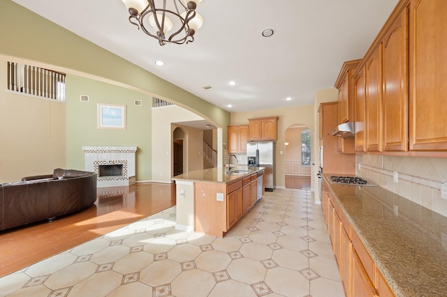 kitchen with pendant lighting, stainless steel fridge, backsplash, a center island with sink, and a tiled fireplace