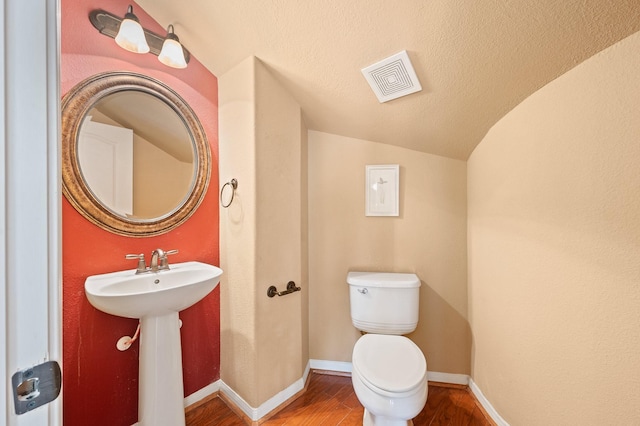 bathroom featuring toilet, sink, vaulted ceiling, a textured ceiling, and hardwood / wood-style flooring